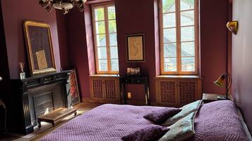 A room with a large bed, a fireplace, and two windows with curtains.