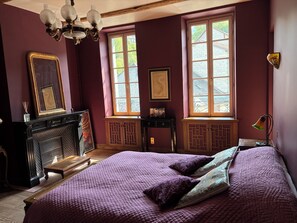 A room with a large bed, a fireplace, and two windows with curtains. - Maison Crone (Castillon-en-Couserans)