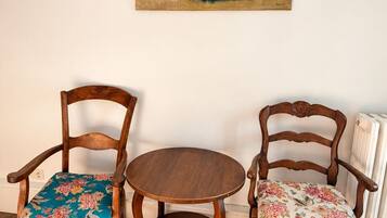 A room with two wooden chairs with floral upholstery and a small round table. A painting of flowers hangs on the wall.
