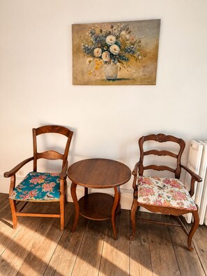 A room with two wooden chairs with floral upholstery and a small round table. A painting of flowers hangs on the wall. - Maison Crone (Castillon-en-Couserans)