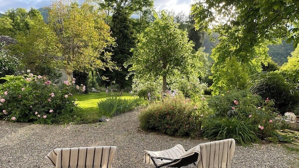 An outdoor seating area with two chairs and a table, surrounded by lush greenery and flowering plants. - Maison Crone (Castillon-en-Couserans)