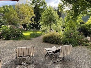 An outdoor seating area with two chairs and a table, surrounded by lush greenery and flowering plants.