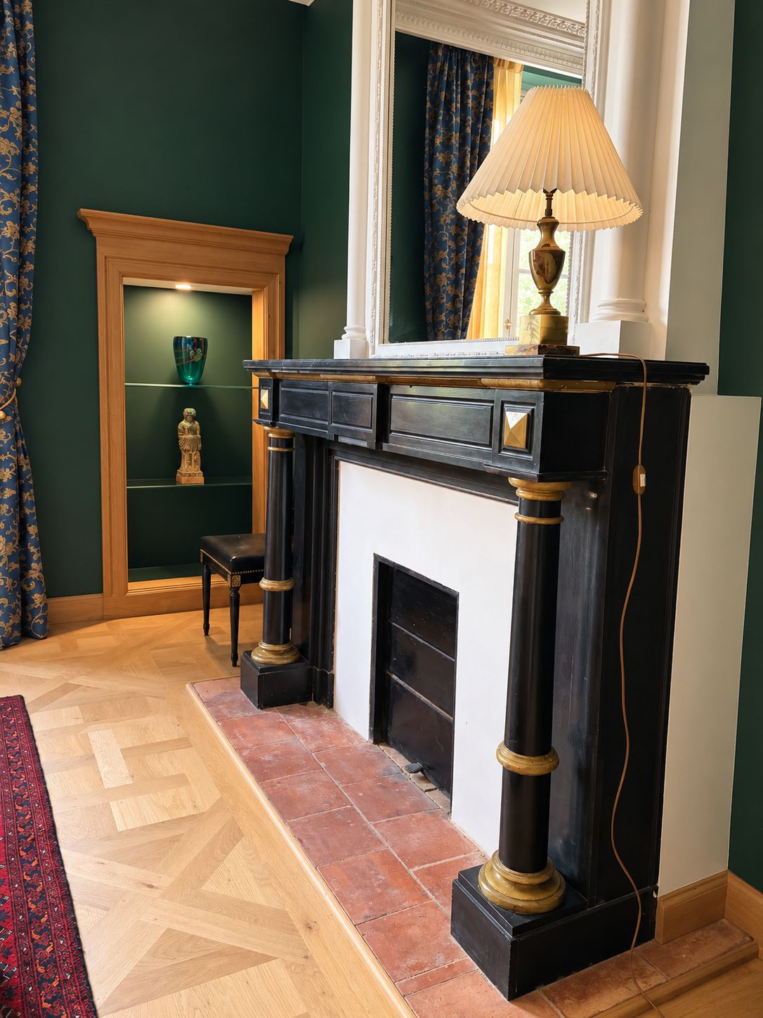 Una habitación con chimenea, una lámpara, un sillón y una estantería con adornos.