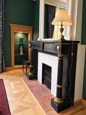 A room with a fireplace, a lamp, a chair, and a shelf with decorative items.