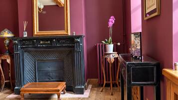 A room with a fireplace, a mirror, a potted orchid, and a wooden floor.