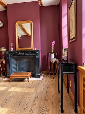 A room with a fireplace, a mirror, a potted orchid, and a wooden floor.