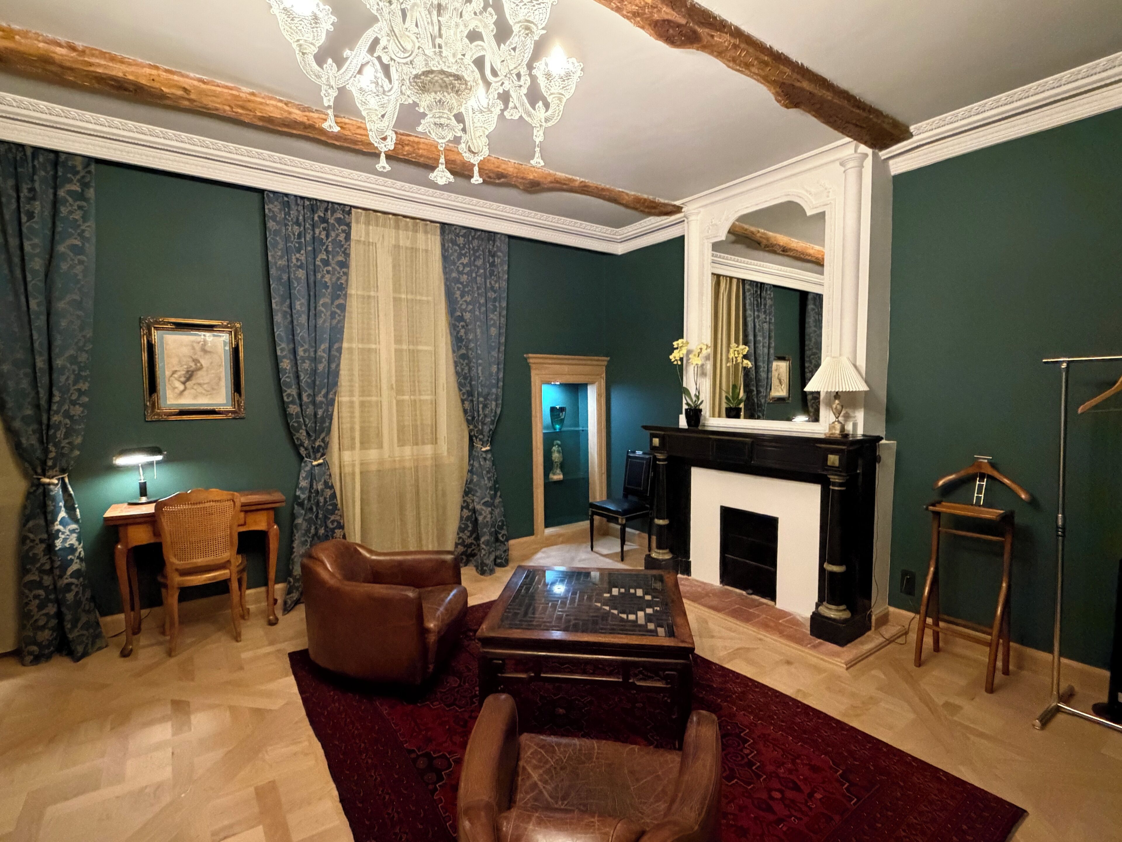 A room with a fireplace, a chandelier, a desk, and a large mirror.