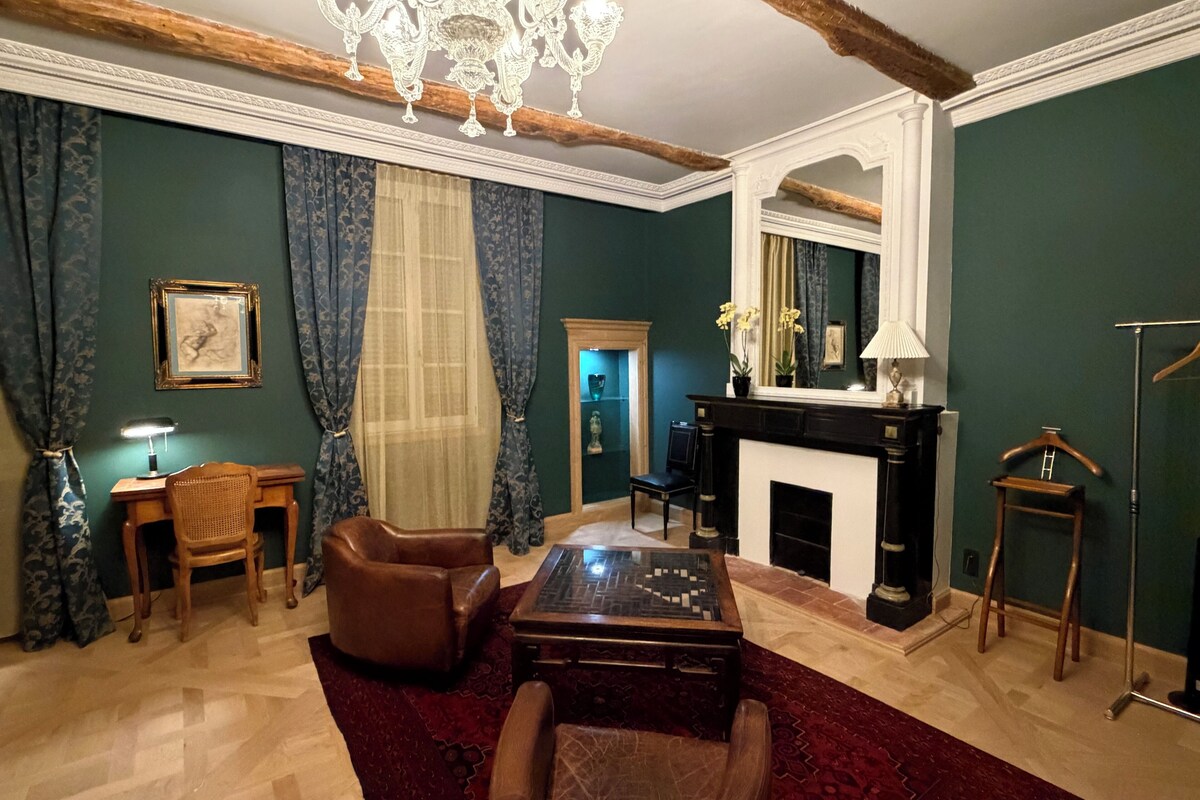 Une pièce avec une cheminée, un lustre, un bureau et un grand miroir.