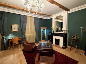 A room with a fireplace, a chandelier, a desk, and a large mirror.