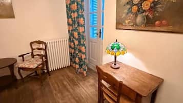 Une pièce avec un plancher en bois, une table avec une lampe, une chaise, un radiateur et une porte avec des volets bleus.