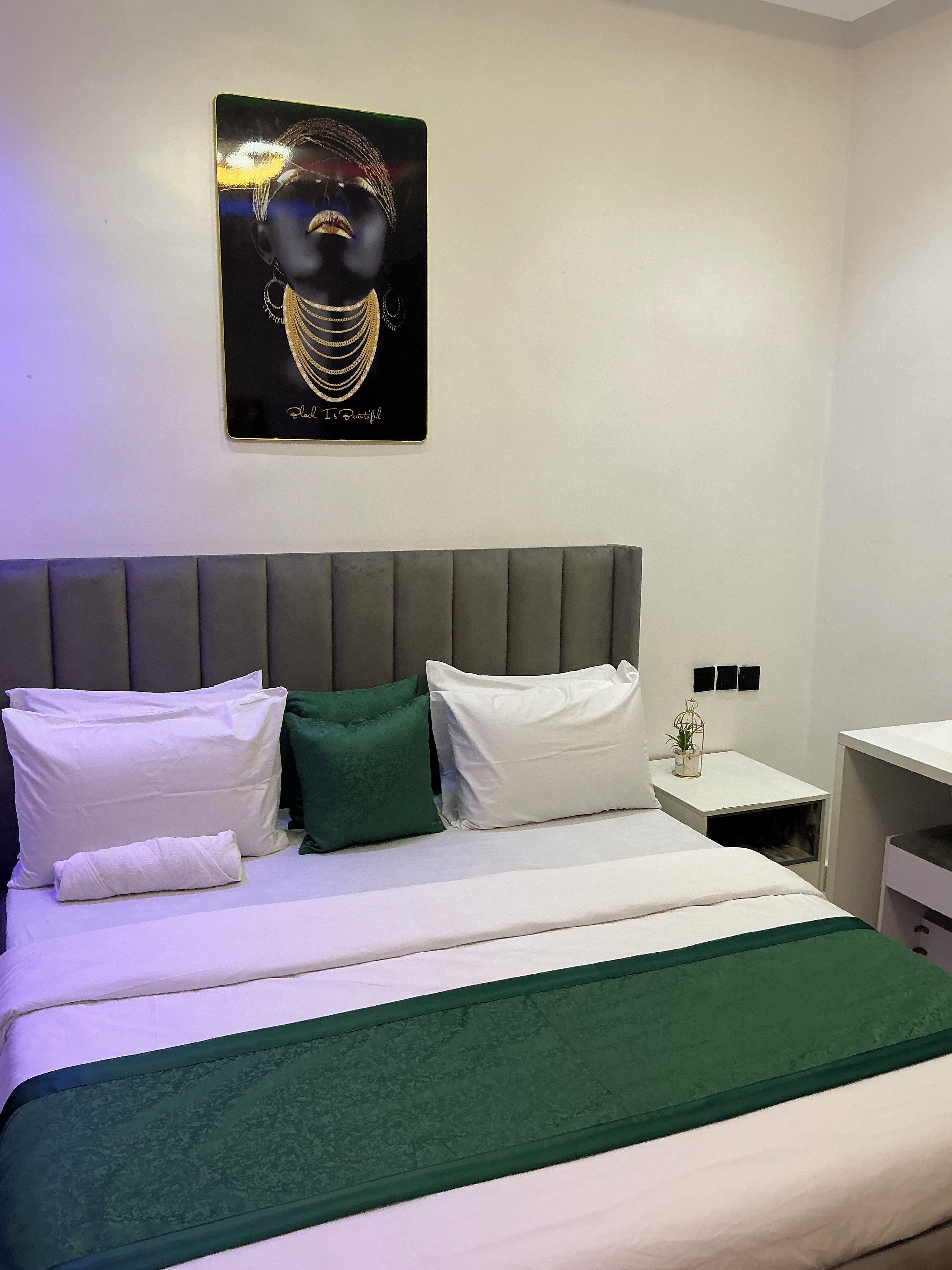 A hotel room with a bed, pillows, a bedside table, a nightstand, and a wall-mounted artwork.