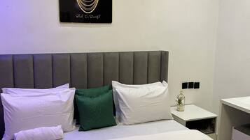 A hotel room with a bed, pillows, a bedside table, a nightstand, and a wall-mounted artwork.