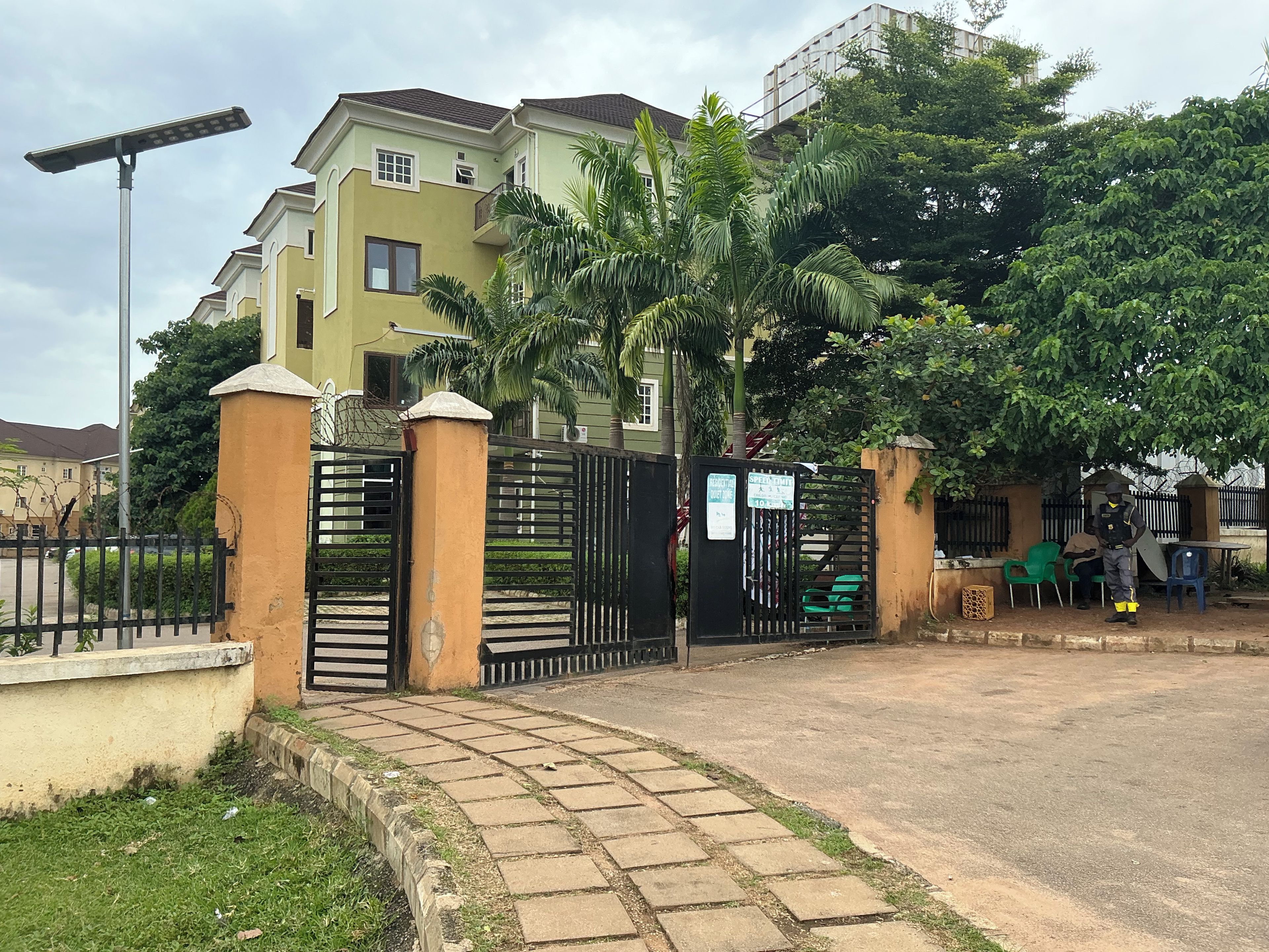 A gated residential area with a paved entrance, a solar street light, and a security guard.