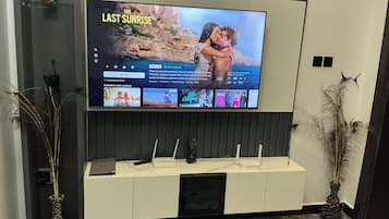 A flat-screen TV mounted on a wall above a white entertainment unit with a remote control, a speaker, and decorative items.