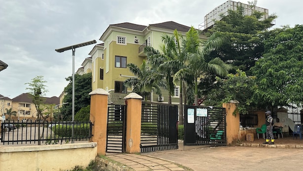 A gated residential area with a paved entrance, a streetlight, and a building with multiple windows and balconies. - Lexrach Luxury Apartments (Abuja)