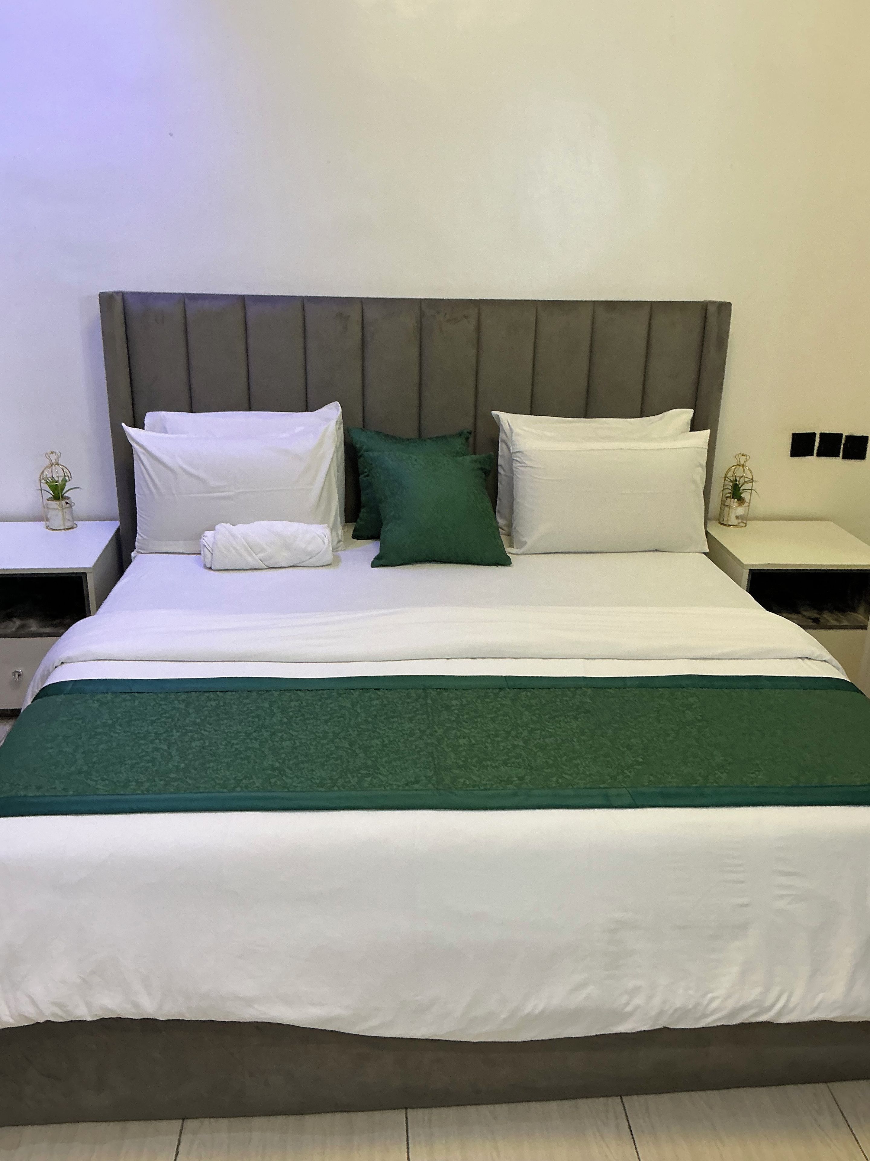 A neatly made bed with a grey headboard, white and green pillows, and a green bedspread.