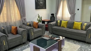A living room with two grey sofas, a glass coffee table, and a painting on the wall. - Lexrach Luxury Apartments (Abuja)