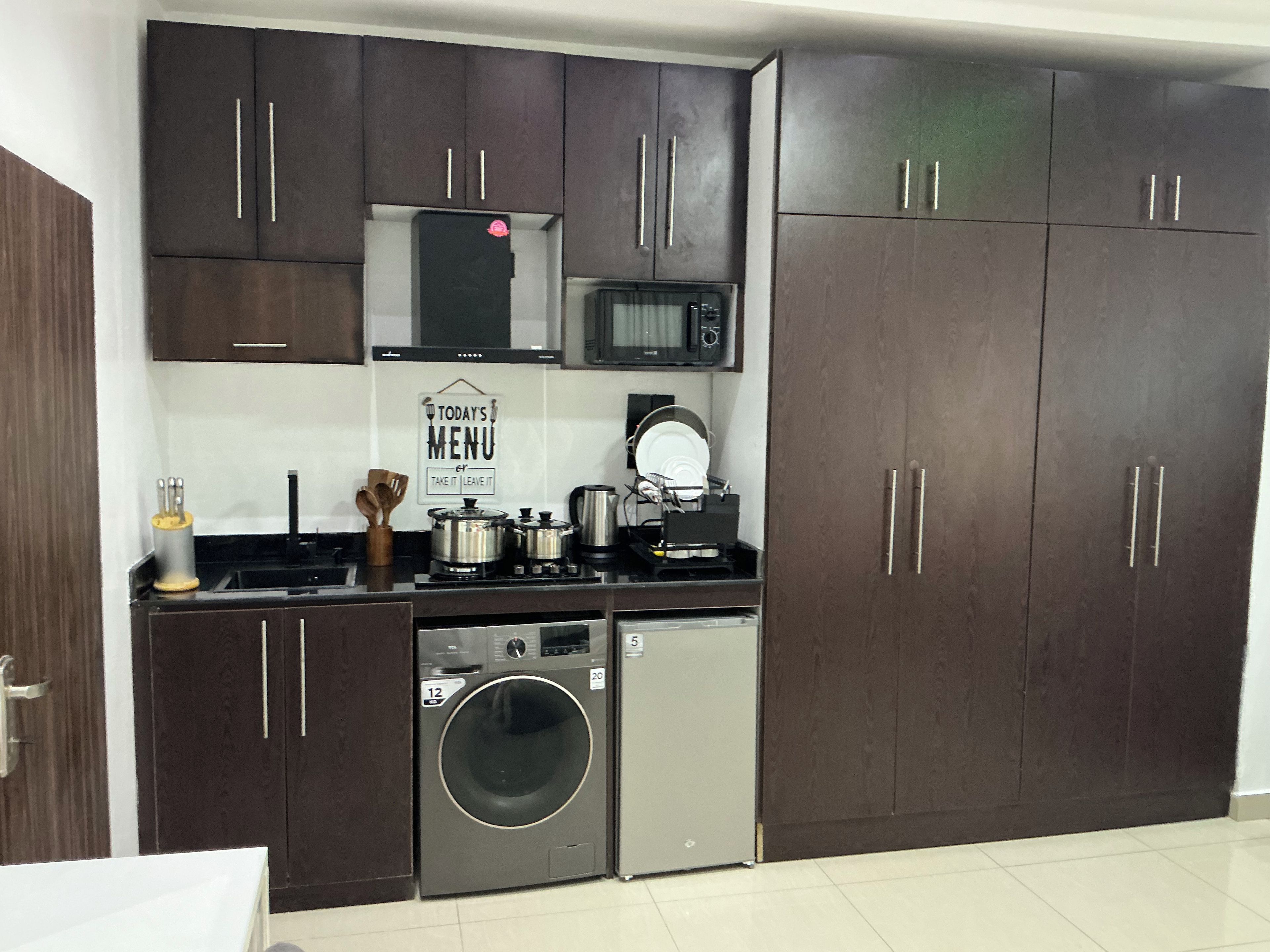 A compact kitchen with dark cabinets, a microwave, a washing machine, and a coffee maker.