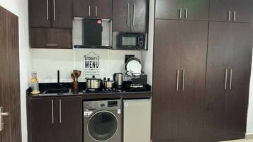 A compact kitchen with dark cabinets, a microwave, a washing machine, and a coffee maker.