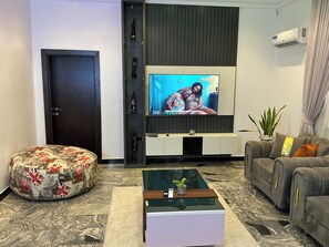 A modern living room with a flat-screen TV, a sofa, a coffee table, and a decorative ottoman. - Lexrach Luxury Apartments (Abuja)