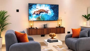 Een moderne woonkamer met twee grijze banken, een salontafel, een aan de muur bevestigde televisie en een houten kastje eronder.