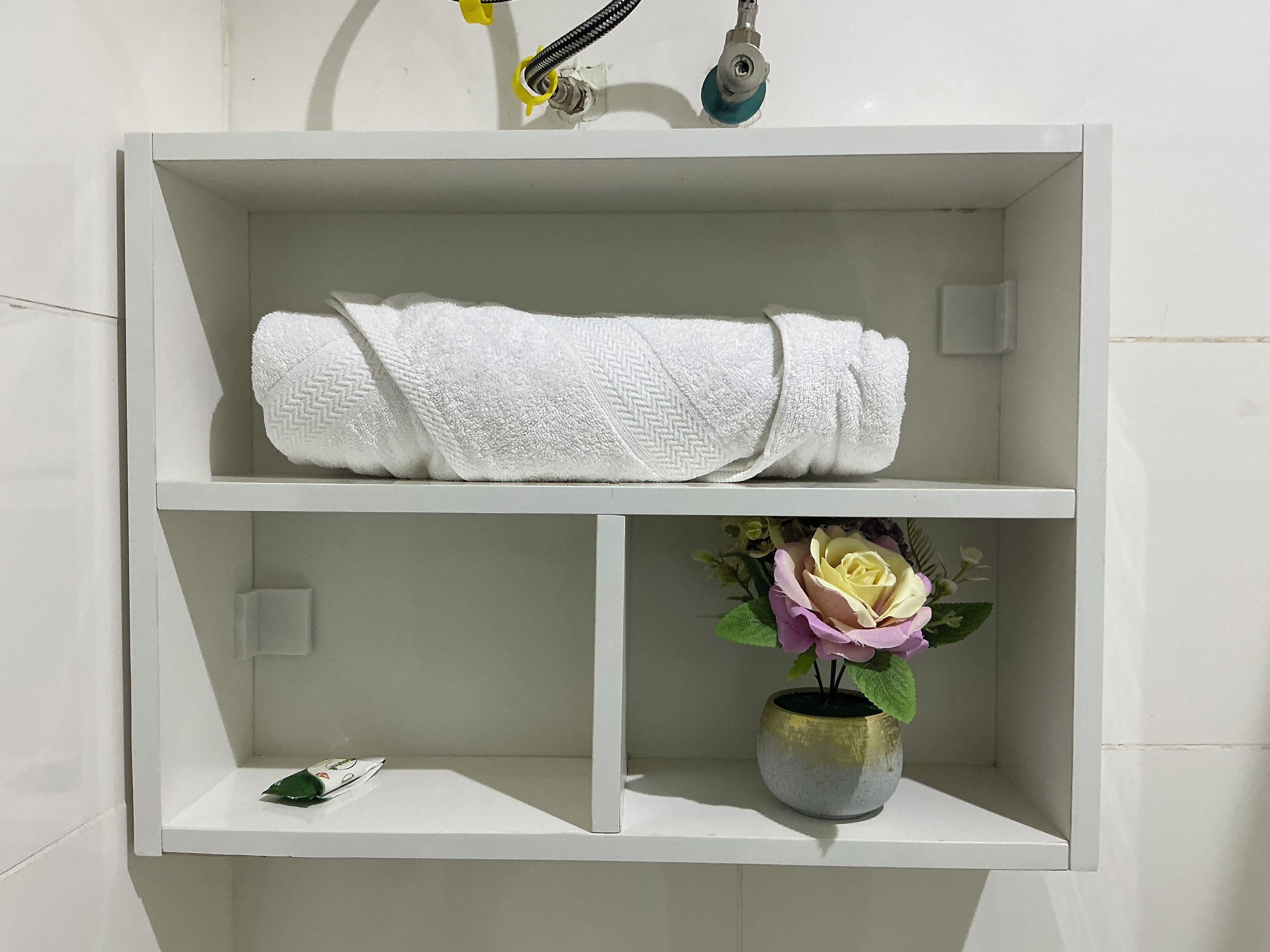Ein weißes Regal mit einem gefalteten weißen Handtuch und einer Vase mit einer einzelnen Blume.