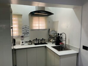 A compact kitchen with white cabinets, a built-in stove, a sink, and a window with blinds. - Lexrach Luxury Apartments (Abuja)