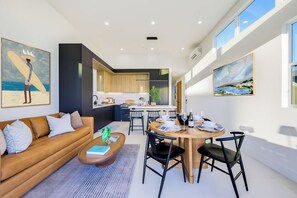 A modern living space with a sofa, coffee table, dining area, and kitchen. - Pacific Sunset House  - Rooftop, Bay Views (San Diego)