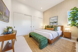 A modern bedroom with a large bed, a desk, and a green bench. - Pacific Sunset House  - Rooftop, Bay Views (San Diego)