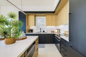 A modern kitchen with dark cabinetry, a central island, and a potted plant. - Pacific Sunset House  - Rooftop, Bay Views (San Diego)