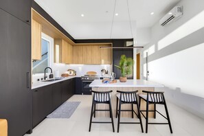 A modern kitchen with dark cabinetry, a central island, and bar stools. - Pacific Sunset House  - Rooftop, Bay Views (San Diego)