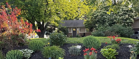 A residential property with a well-maintained garden, a small house with a front door, and a driveway.