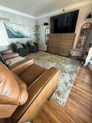 A living room with a brown leather sofa, a wooden cabinet, a flat-screen TV, and a large abstract painting on the wall.