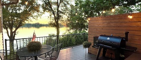 An outdoor deck with a table and chairs, a grill, and string lights.