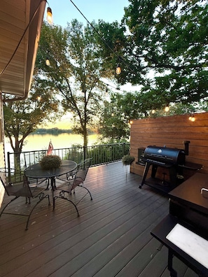 An outdoor deck with a table and chairs, a grill, and string lights.
