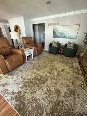 Un soggiorno con un divano in pelle marrone, una poltrona verde, un tappeto decorato e un quadro appeso al muro.