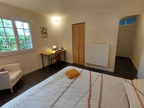Ein Schlafzimmer mit Bett, Schreibtisch, Stuhl, Heizkörper und einem Fenster mit Blick auf Grünflächen.