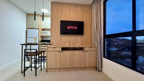Eine moderne Küche mit integriertem Fernseher, der 'NETFLIX' anzeigt, und einem Essbereich mit Stühlen und Tisch.