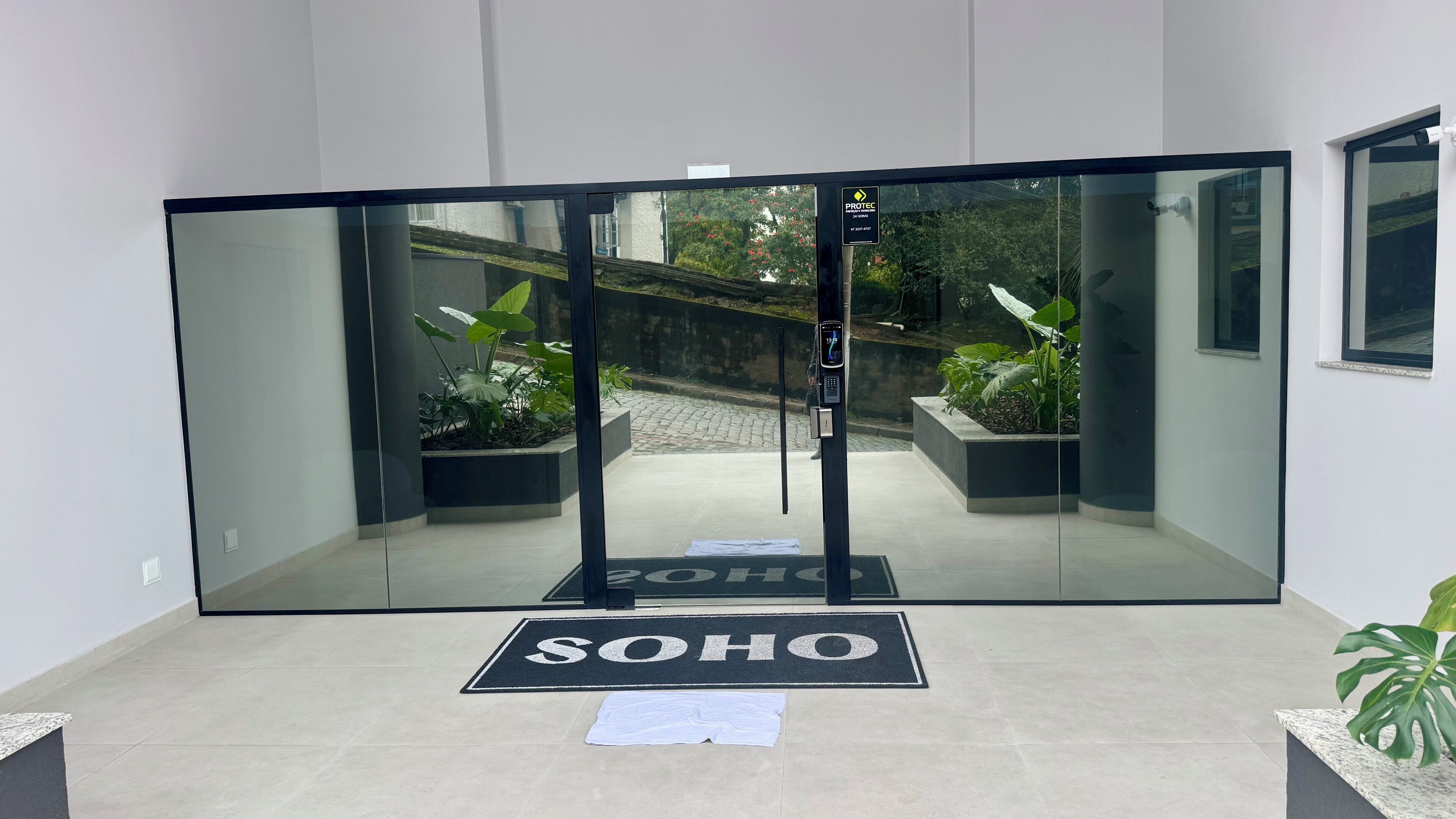 Ein moderner Eingangsbereich mit Glastür, einem 'SOHO'-Schild und Kübelpflanzen.