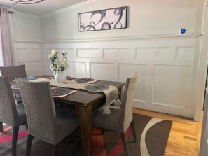 Comedor con mesa de madera dispuesta para cuatro personas, sillas tapizadas, un jarrón con flores y una obra de arte abstracto colgada en la pared.