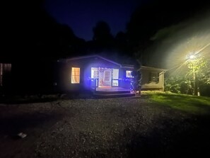 Una casa con porche iluminada por luces azules, rodeada por un camino de grava.
