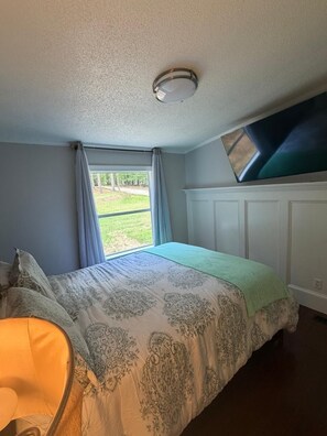 Ein Schlafzimmer mit einem Bett, einem Fenster, einer Deckenleuchte und einem an der Wand befestigten Fernseher.