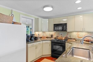 A kitchen with white cabinets, a black stove, a microwave, and a stainless steel sink. - The Gatsby House - Ocean View - Steps to Beach - 8BR 6BA (Murrells Inlet)