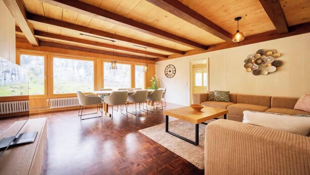 Un salon spacieux avec un plafond en bois, un coin repas avec des chaises, un canapé et une table basse.