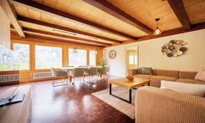 A spacious living room with a wooden ceiling, a dining area with chairs, a sofa, and a coffee table.