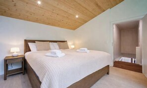 A bedroom with a wooden ceiling, a bed with white bedding, two bedside lamps, and a neatly made bed with folded towels. - MODERN CHALET RETREAT WITH ICONIC LAUTERBRUNNEN VIEWS (Lauterbrunnen)