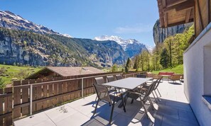 An outdoor patio with a table and chairs, overlooking a mountainous landscape with a wooden cabin in the background. - MODERN CHALET RETREAT WITH ICONIC LAUTERBRUNNEN VIEWS (Lauterbrunnen)