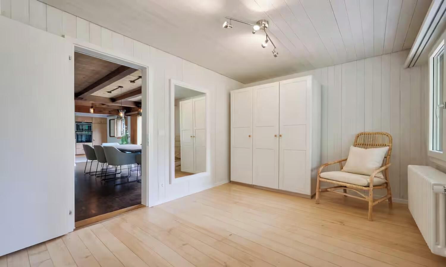 A spacious room with a wooden floor, a wicker chair, and a white wardrobe.