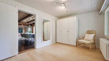 A spacious room with a wooden floor, a wicker chair, and a white wardrobe.