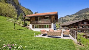 Ein modernes Chalet mit Balkon, umgeben von einer üppigen grünen Rasenfläche und einem Bergpanorama.